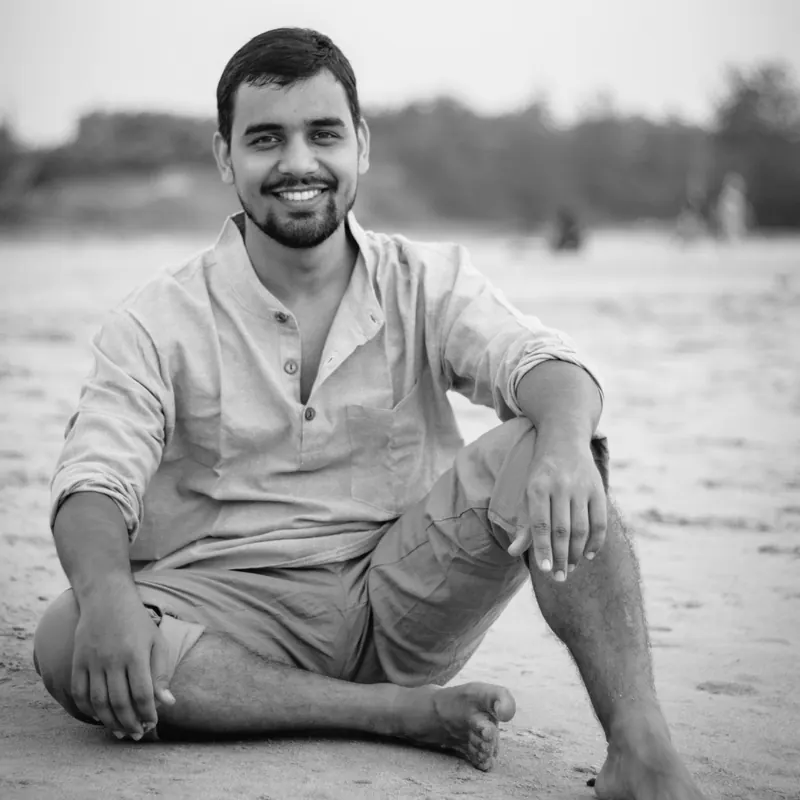 Himanshu Bisht sitting barefoot on a beach, smiling
